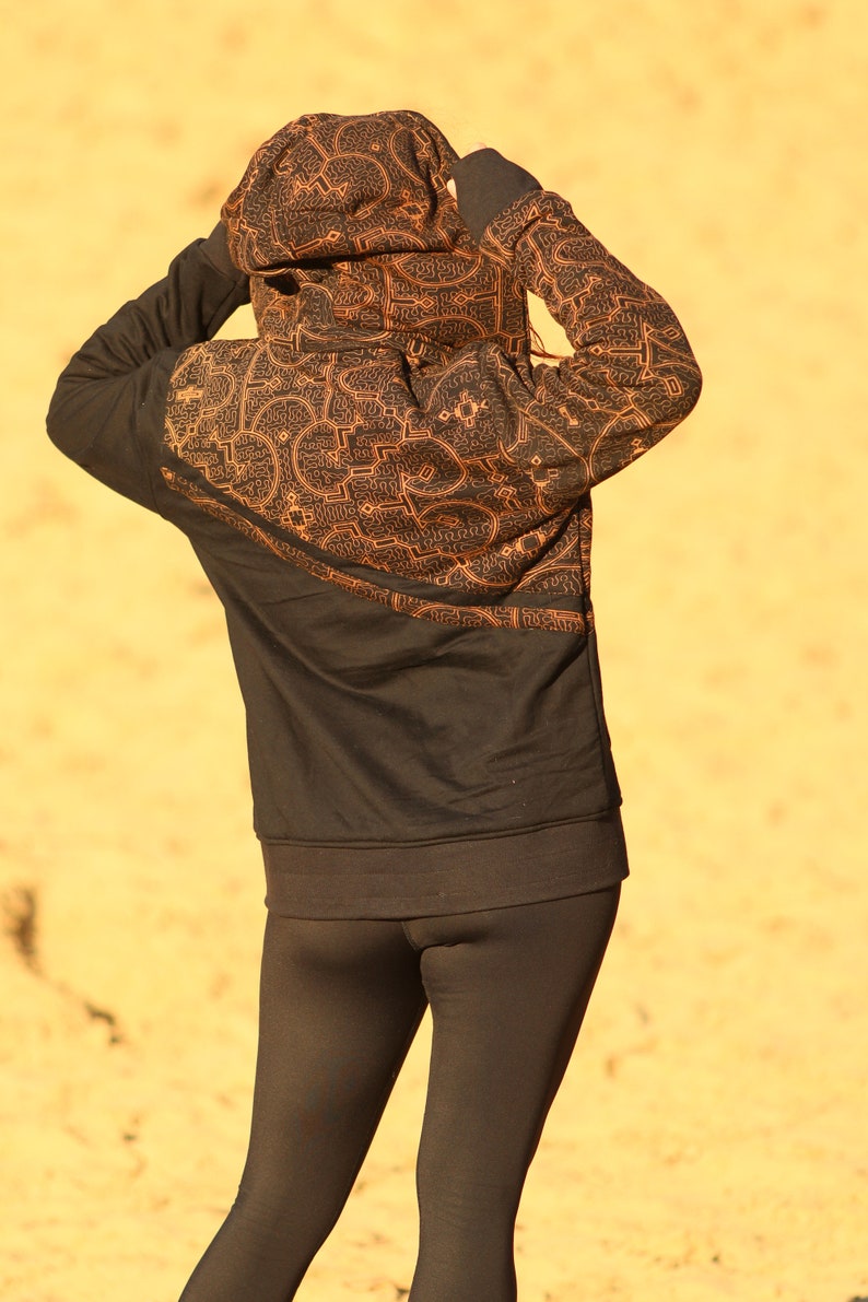 May include: A black hoodie with a geometric pattern in orange. The hoodie is worn by a person with black leggings.