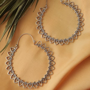 May include: A pair of silver hoop earrings with a delicate, intricate design. The earrings are circular and feature a scalloped edge with small, round accents.