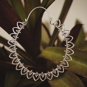 May include: Silver hoop earrings with a delicate, scalloped design. The earrings are circular and have a textured finish.