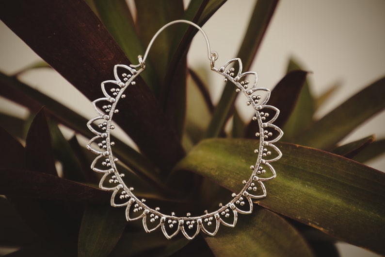 May include: Silver hoop earrings with a delicate, scalloped design. The earrings are circular and have a textured finish.