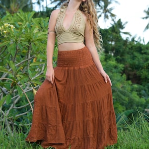 May include: A two-piece outfit featuring a halter top and a tiered maxi skirt. The halter top is a light olive green with a crochet design. The skirt is a rust-colored, flowing maxi skirt, perfect for a bohemian style.