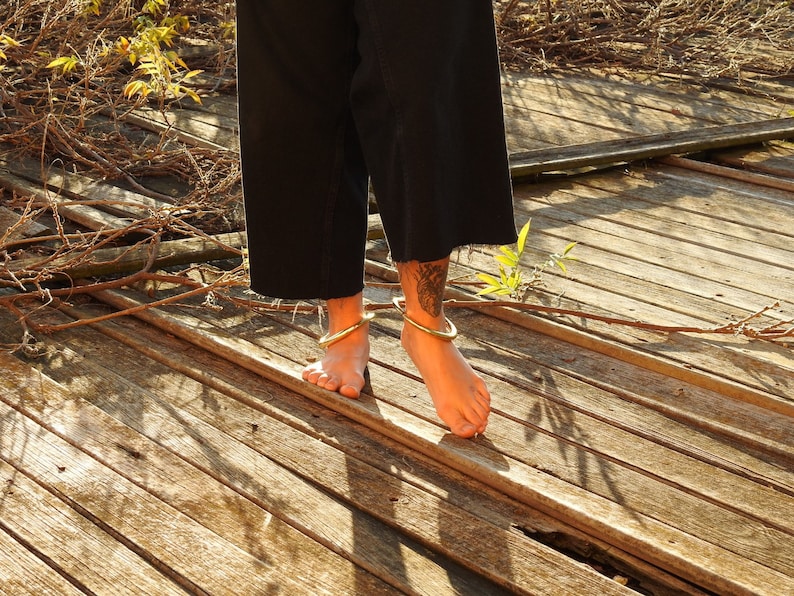 K&ouml;nnte beinhalten: Eine Person in schwarzen Hosen und goldenen Fu&szlig;kettchen steht auf einer Holzplattform. Die Plattform besteht aus verwitterten Holzdielen.