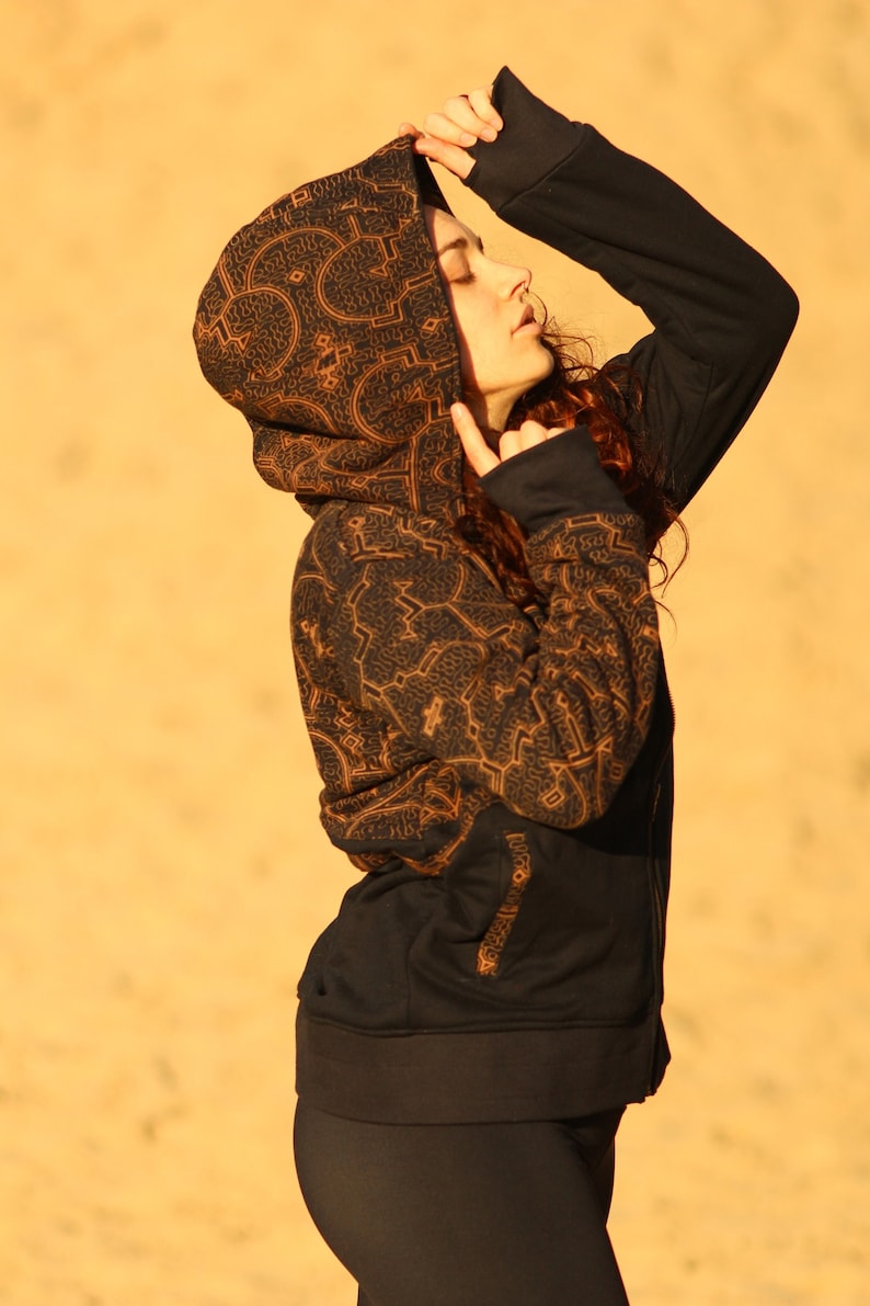 May include: A black hooded sweatshirt with a brown geometric pattern. The hood is pulled up over the person's head.