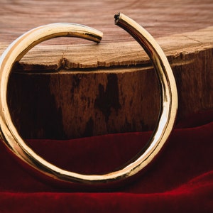K&ouml;nnte beinhalten: Ein dicker goldener Metallring, leicht verbogen, liegt auf einer Holzoberfl&auml;che mit einem roten Samtstoff im Vordergrund.