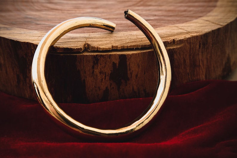 K&ouml;nnte beinhalten: Ein dicker goldener Metallring, leicht verbogen, liegt auf einer Holzoberfl&auml;che mit einem roten Samtstoff im Vordergrund.