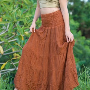 May include: A rust-colored, tiered maxi skirt with a smocked waistband. The skirt is paired with a halter top in a light olive green color. The outfit is suitable for casual wear and is made of a lightweight fabric.