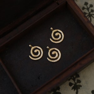 Op de afbeelding: Drie goudkleurige metalen spiraalcharms in een houten doos. De charms zijn rond en hebben een verhoogd spiraalontwerp.