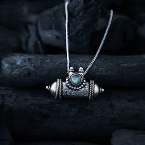 Peut inclure: Un collier en argent avec un pendentif en argent orné d'un motif complexe et d'une pierre précieuse bleue. Le collier est présenté sur un fond sombre.