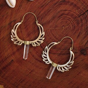 May include: A pair of gold hoop earrings with a crystal pendant hanging from each hoop. The hoops are decorated with a delicate, leaf-like design.