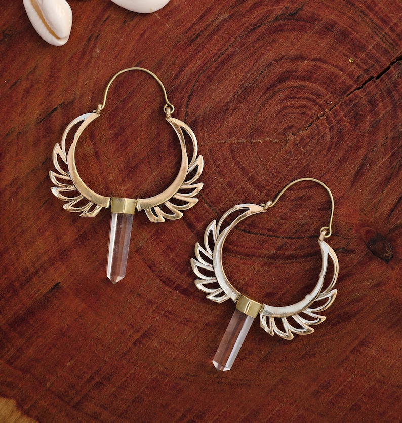May include: A pair of gold hoop earrings with a crystal pendant hanging from each hoop. The hoops are decorated with a delicate, leaf-like design.