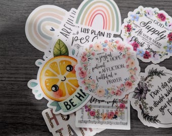 May include: A collection of colorful stickers with various designs. One sticker features a smiling orange slice with the words "BE HAPPY". Other stickers include floral wreaths and inspirational quotes. A rainbow sticker is also visible.
