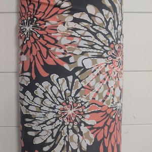 May include: A roll of fabric featuring a large floral pattern. The design includes coral, white, and tan flowers on a dark gray background. The fabric is tightly rolled, showcasing the repeating pattern.