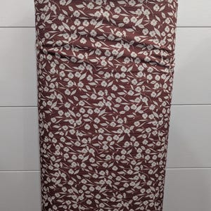 May include: A roll of fabric featuring a repeating floral pattern. The fabric has a deep burgundy background with a delicate pattern of small white flowers and leaves. The fabric is tightly rolled, showcasing the detailed design.