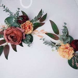 May include: Two floral arrangements featuring burgundy, peach, and green silk flowers. The arrangements are crafted with artificial greenery and are ideal for bringing a touch of nature to any setting.