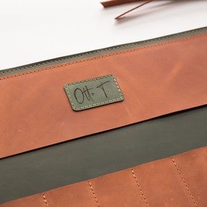 May include: A green leather tool roll with a brown leather flap. The flap has a small, rectangular leather patch with the text "Ott T." stitched in black.
