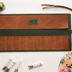 May include: A green leather roll-up case with brown leather pockets and a strap. The case is open and has eight slots for paint tubes. The case has the text "Oil T" on the front.