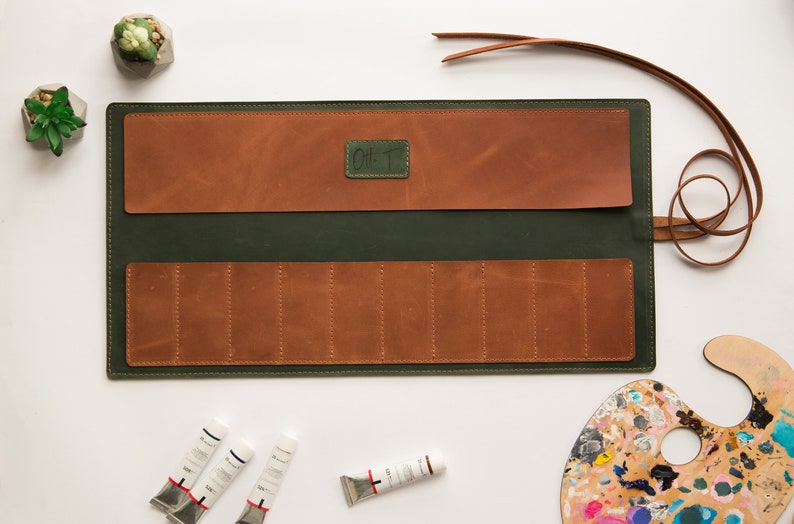 May include: A green leather roll-up case with brown leather pockets and a strap. The case is open and has eight slots for paint tubes. The case has the text "Oil T" on the front.