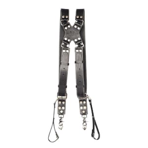 May include: A black leather harness featuring an X-shaped back panel with white stitching and silver-toned metal rivets. The harness includes adjustable straps, metal buckles, and swivel snap hooks at the bottom ends. The text "MATTINA MARINA" is embossed on the center back panel.