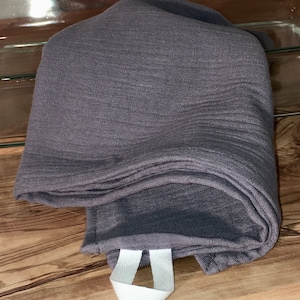 Könnte beinhalten: Ein dunkelgraues Geschirrtuch mit einem weißen Schlaufe. Das Handtuch ist gefaltet und scheint aus einem weichen, strukturierten Stoff zu sein.