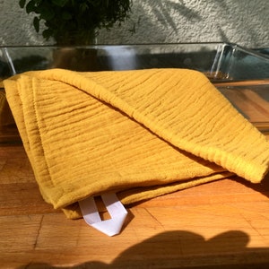 May include: A folded, mustard-yellow kitchen towel with a textured, crinkled surface. A white fabric loop is attached to the corner. The towel rests on a wooden cutting board next to a clear glass baking dish.