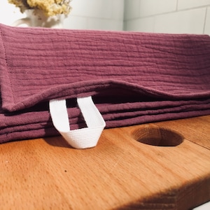 May include: A folded purple cotton dish towel with a white cotton loop handle. The towel is lying on a wooden surface.