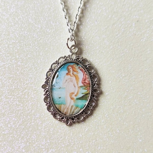 A silver oval jewellery charm, with a photo of Botticelli's Birth of Venus painting. Attached to a silver chain, against a creamy, sparkly background.