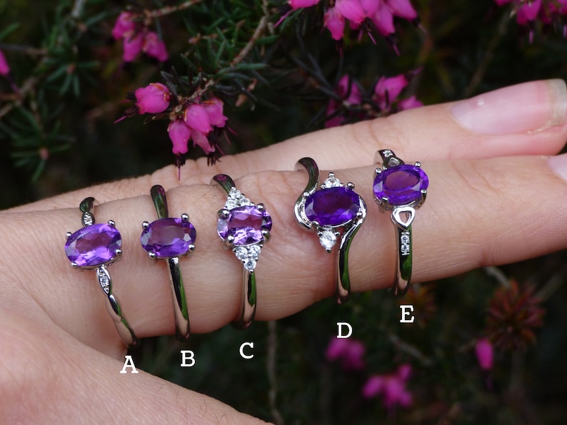 May include: Five silver rings with oval amethyst gemstones and small clear cubic zirconia accents. The rings are labeled A through E.