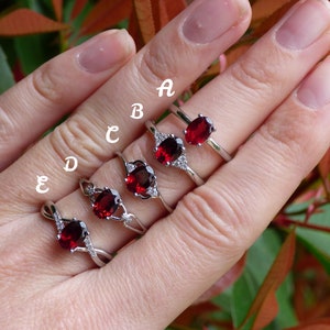 May include: Five silver rings with red oval gemstones and clear cubic zirconia accents. The rings are labeled A through E.