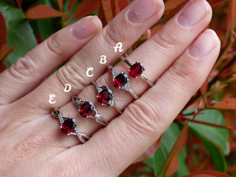 May include: Five silver rings with red oval gemstones and clear cubic zirconia accents. The rings are labeled A through E.