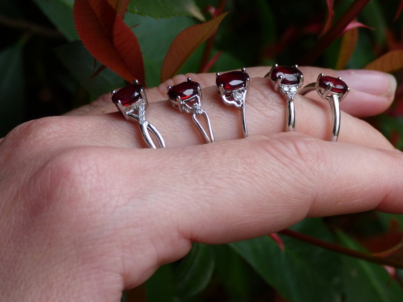 May include: Five silver rings with red gemstones and small clear stones. The rings are arranged in a row on a hand, with the largest ring on the pinky finger and the smallest ring on the thumb.