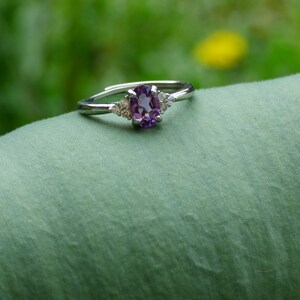 May include: A silver ring with a purple oval gemstone and two smaller clear gemstones on the band.