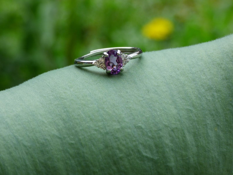 May include: A silver ring with a purple oval gemstone and two smaller clear gemstones on the band.