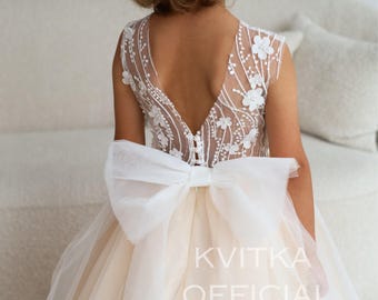 Op de afbeelding: Een mouwloze jurk met een transparante achterkant met witte bloemenborduursels en een diepe V-hals. Een grote witte organza strik is bevestigd in de taille boven een gelaagde tule rok. De tekst KVITKA OFFICIAL is zichtbaar aan de rechterkant.