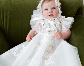 Può includere: Un abito da battesimo bianco con dettagli in pizzo intricato sul corpetto, maniche trasparenti con volant e una gonna in tulle a strati con ricami floreali. L'outfit include una cuffietta abbinata con bordo in pizzo e il testo KVITKA OFFICIAL.