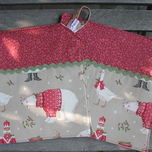 Könnte beinhalten: Zwei weihnachtliche Ofenhandschuhe. Der obere Teil hat ein rotes Blumenmuster mit einem grünen, gewellten Rand. Der untere Teil zeigt einen beigen Hintergrund mit Illustrationen von Gänsen, einem Eisbären in einem roten Pullover und Spielzeugsoldaten.