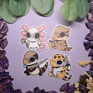 Op de afbeelding: Vier cartoon stickers met verschillende dieren die wapens vasthouden. De eerste sticker is roze en wit en toont een axolotl die een bijl vasthoudt. De tweede sticker is bruin en toont een hagedis die een aansteker vasthoudt. De derde sticker is bruin en wit en toont een hagedis die een zwaard vasthoudt. De vierde sticker is geel en bruin en toont een gekko die een mes vasthoudt.