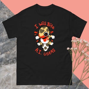 Könnte beinhalten: Schwarzes T-Shirt mit einem Cartoon-Kreaturen-Design. Die Kreatur hat einen herzförmigen Kopf und einen blutigen Mund. Roter Text oben und unten lautet "I will Bite A.I. users". Das Design ist auf dem T-Shirt zentriert.