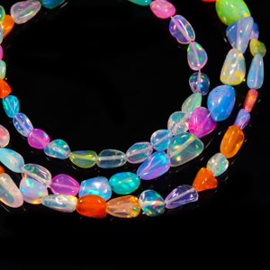 Puede incluir: Una hebra de cuentas de piedras preciosas de ópalo de colores en varias formas y tamaños. Las cuentas son iridiscentes y reflejan la luz en un arcoíris de colores.