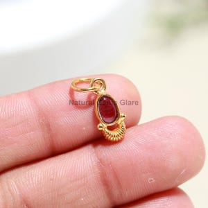 Pode incluir: Pingente de ouro com uma gema vermelha. O pingente tem um design detalhado com um pequeno laço na parte superior para prender a uma corrente.