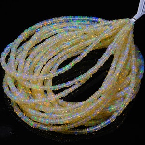 Op de afbeelding: Een streng witte opaal kralen met iriserende regenboogkleuren. De kralen zijn klein en rond en zijn geregen op een doorzichtige draad. De kralen zijn gerangschikt in een losse spiraal.