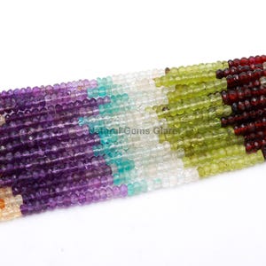 Può includere: Fili di perline di pietre preziose sfaccettate in un arcobaleno di colori. Le perline sono disposte in file, mostrando tonalità di viola, blu, verde, giallo e rosso. Le perline sono piccole e rotonde, con una finitura lucida.