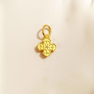 May include: A gold-coloured pendant in the shape of a cross with intricate floral designs. The pendant has a small loop at the top for attaching to a chain. The cross is displayed against a white background.