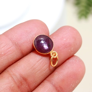 Op de afbeelding: Een gouden hanger met een ronde, cabochon geslepen robijn edelsteen. De robijn is diep rood van kleur met een lichte glans.