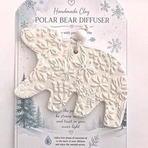 May include: A white clay polar bear diffuser with an embossed floral pattern, suspended by a string with a white bead. It is mounted on a card labelled Handmade Clay POLAR BEAR DIFFUSER, featuring a winter forest scene and instructions to add essential oil to the back.