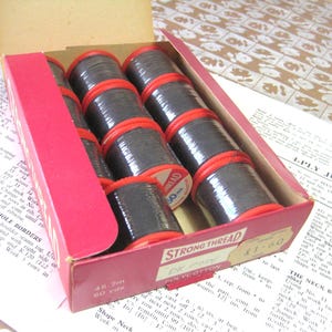 May include: A box of black Strong Thread Polycotton sewing thread spools. The box is red and white with the text "Strong Thread Polycotton" and a price tag of £1.80.