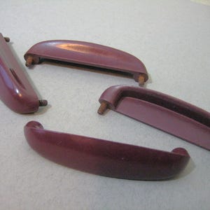 May include: Four burgundy plastic drawer pulls with screw holes. The pulls are all different sizes and shapes.
