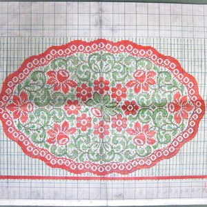 May include: A red and green floral embroidery pattern on a white gridded background. The pattern is a circular design with a scalloped edge.