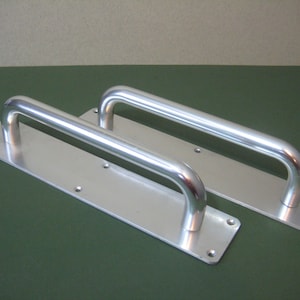 May include: Two silver door handles with a rectangular backplate. The handles are made of metal and have a smooth, polished finish.