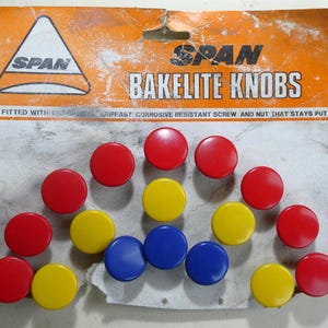 May include: A selection of SPAN Bakelite knobs in red, yellow, and blue. The knobs are circular and have a smooth, shiny surface. The packaging is orange and white, displaying the brand name and product details.