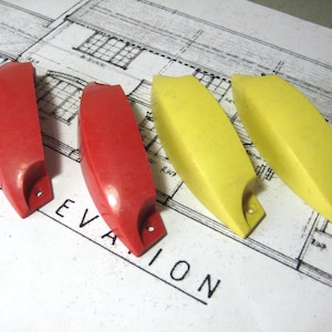 May include: Four plastic drawer pulls, two red and two yellow. The pulls are shaped like a curved rectangle with a rounded end.